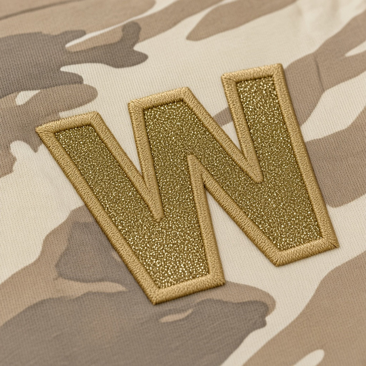 Close-up of the gold embroidered appliqué W on natural camo